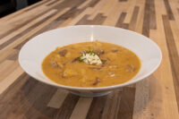 Bowl of Frankfurt Soup Frankfurtská Polévka with a sour cream dollop and chive garnish on a wooden table.