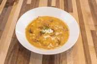 Bowl of Frankfurt Soup Frankfurtská Polévka with meat chunks, potatoes, sour cream, and chives on wood table.
