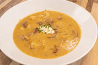Bowl of Frankfurt Soup Frankfurtská Polévka with sausage chunks, sour cream dollop, and chives.