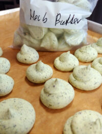 Herb Butter Piped mounds of herb butter on parchment paper with a bag labeled 'Herb Butter' in the background.