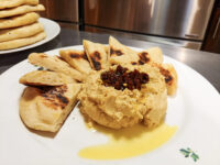 Hummus Hummus mounded on a plate, topped with a dark relish and olive oil, ringed by grilled flatbread wedges.