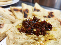 Hummus Bowl of hummus topped with chopped sun-dried tomatoes and olive oil, served with grilled pita triangles.