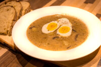 Bowl of Kulajda Soup with mushrooms and potatoes, topped with a halved soft-boiled egg, served with bread.