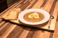 Bowl of Kulajda Soup topped with halved soft-boiled eggs, served with crusty bread on a wooden board.