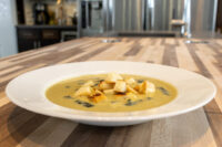 Leek Soup A white bowl of Leek Soup topped with golden croutons, set on a wooden countertop.