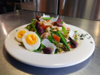 Niçoise Salad with Tuna Niçoise Salad with Tuna on a white plate with green beans, olives, tomato, cheese shavings, and a halved egg.