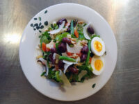 Niçoise Salad with Tuna Niçoise Salad with Tuna on a white plate with egg, green beans, kalamata olives and shaved cheese.
