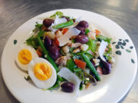 Niçoise Salad with Tuna Niçoise Salad with Tuna on a leaf-patterned plate with green beans, olives, egg halves, and shaved cheese.