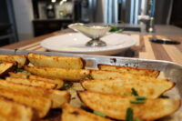 Oven-Roasted Potato Wedges Crispy Oven-Roasted Potato Wedges topped with chives on a metal tray, gravy boat blurred behind.