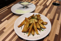 Oven-Roasted Potato Wedges Crispy Oven-Roasted Potato Wedges topped with chives, served beside a gravy boat of pale green dip.