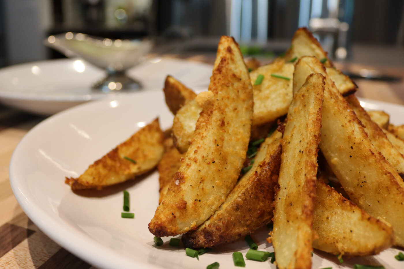 Oven-Roasted Potato Wedges Crispy golden Oven-Roasted Potato Wedges piled on a white plate, topped with chopped chives.