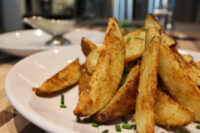 Oven-Roasted Potato Wedges Crispy golden Oven-Roasted Potato Wedges piled on a white plate, topped with chopped chives.