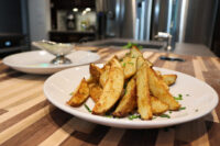 Oven-Roasted Potato Wedges Plate of Oven-Roasted Potato Wedges topped with chives, with a small gravy boat of sauce behind it.