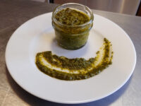 Pesto Glass jar of Pesto with a swoosh of the same sauce drizzled on a white plate.