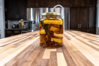 Jar of pickled brie cheese nakládaný hermelín with red onion and herb sprigs steeped in oil on a wooden counter.