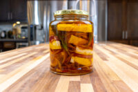 Jar of Pickled Brie Cheese Nakladany Hermelin wedges with onion and herbs in oil, gold lid on wood counter.