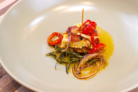 Golden Nakladany Hermelin cheese topped with chili strips and red onion, in oil on a white plate.