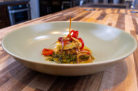 Wedge of Pickled Brie Cheese Nakládaný Hermelín in oil with onion curls and red pepper strips.