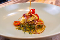 Pickled Brie Cheese Nakladany Hermelin wedges with red pepper, onion, and rosemary in oil on a white plate.