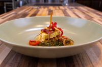 Wedge of Nakladany Hermelin pickled brie topped with red pepper strips in a pool of spiced oil.