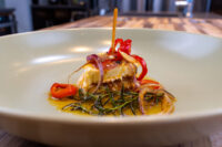 Wedge of Pickled Brie Cheese Nakladaný Hermelín with red onion and chili strips in oil on a plate.