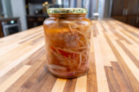 Pickled Sausage Utopenec Glass jar of Pickled Sausage Utopenec with sausage, onions, and red pepper in brine on a wood counter.
