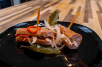 Pickled Sausage Utopenec Sliced Pickled Sausage Utopenec sausage links topped with onion and chili on a black plate.