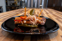 Pickled Sausage Utopenec Pickled Sausage Utopenec: sliced sausages with pickled onions, red pepper strips, and bay leaves on a black plate.