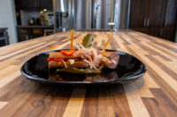 Pickled Sausage Utopenec Skewered pickled sausage pieces with onion and pepper strips, Pickled Sausage Utopenec on a black plate.