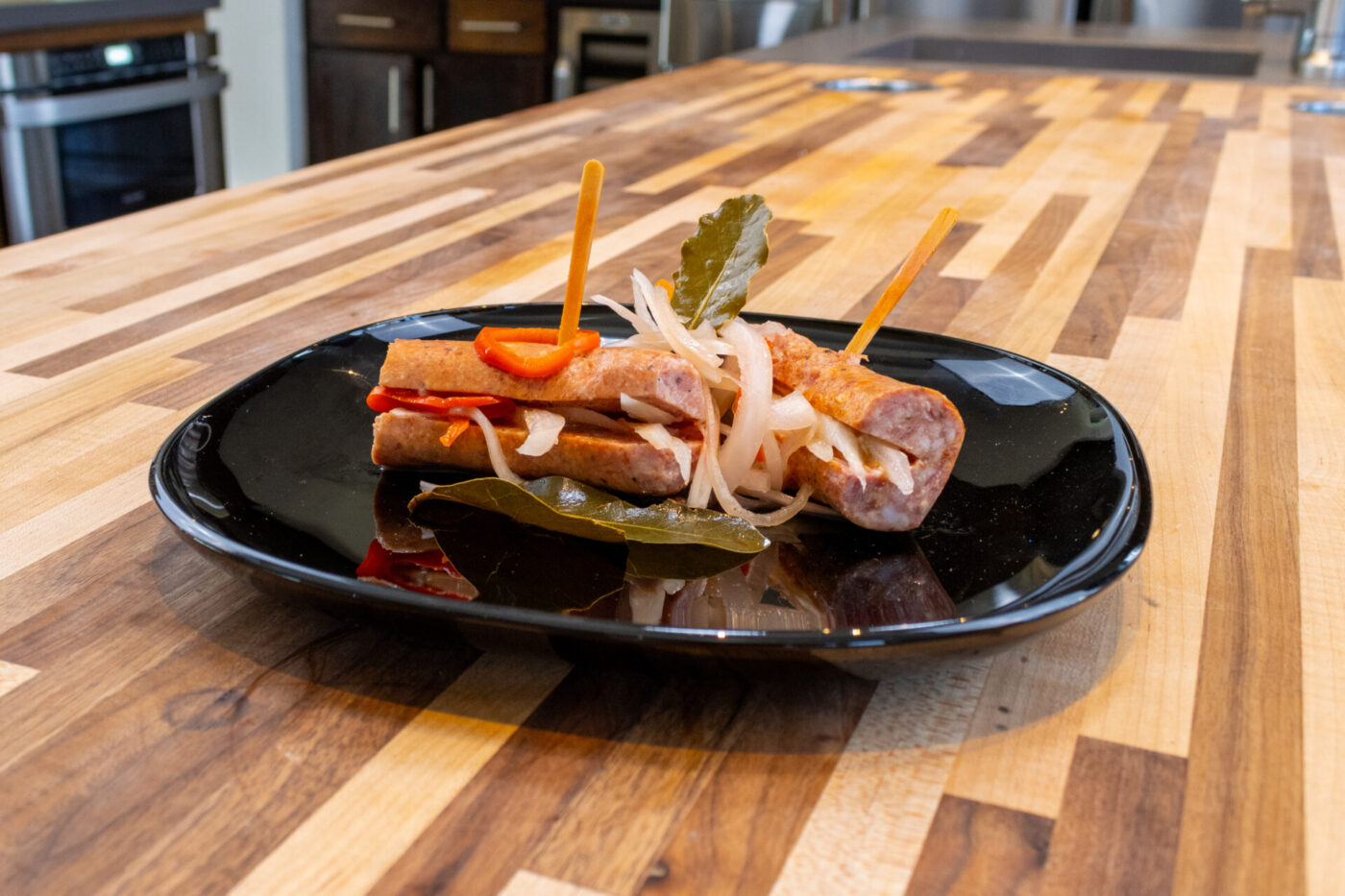 Pickled Sausage Utopenec Pickled Sausage Utopenec with grilled sausage, onions, pepper strips, and bay leaf on a black plate.