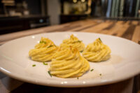 Four piped Potato Kisses Bramborové Pusinky with golden tops and chives on a white plate