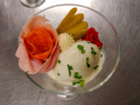 Russian Eggs (Ruské Vejce) Russian Eggs (Ruské Vejce) in a glass with a ham rose, pickle spears, piped cream, and a chive-topped scoop