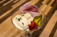 Russian Eggs (Ruské Vejce) Martini glass of Russian Eggs (Ruské Vejce) with egg salad, whipped sauce, ham, roasted pepper, and pickle.