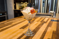 Russian Eggs (Ruské Vejce) Russian Eggs (Ruské Vejce) layered in a martini glass with diced ham and herb garnish on a wood counter.