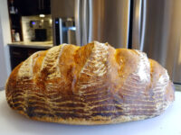 Rustic Bread or Baguettes A round loaf of Rustic Bread or Baguettes with a scored, flour-dusted crust on a white counter.
