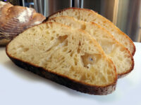 Rustic Bread or Baguettes Three slices of Rustic Bread or Baguettes showing open crumb, with the whole loaf behind them