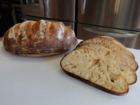 Rustic Bread or Baguettes Whole scored loaf of Rustic Bread or Baguettes beside sliced pieces showing open crumb.