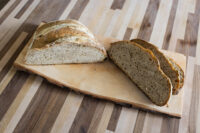 Czech Rye Bread Halved loaf of Czech Rye Bread with several slices cut on a wooden board.