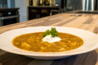 Czech Sauerkraut Soup Zelňačka Bowl of Czech Sauerkraut Soup Zelňačka with diced potatoes, sour cream, and parsley on a wood counter.