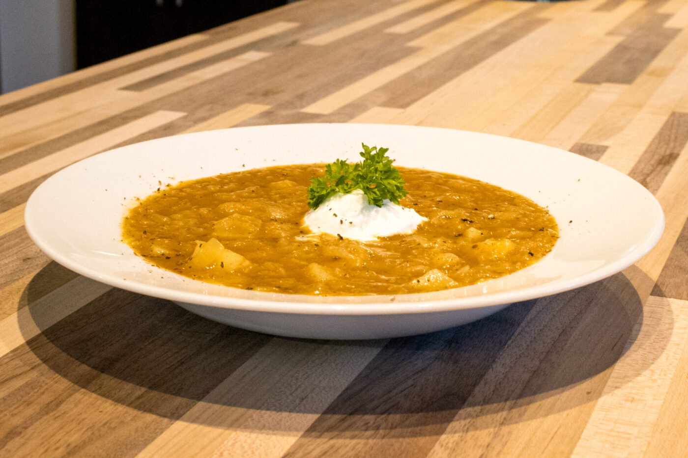 Czech Sauerkraut Soup Zelňačka Bowl of Czech Sauerkraut Soup Zelňačka with diced potatoes, sour cream, and parsley on a wooden table.
