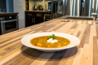 Czech Sauerkraut Soup Zelňačka White bowl of Czech Sauerkraut Soup Zelňačka with orange broth, diced pieces, sour cream, and parsley on a wood counter.
