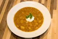 Czech Sauerkraut Soup Zelňačka Bowl of Czech Sauerkraut Soup Zelňačka with diced potatoes, sour cream dollop, and parsley on a wooden table.