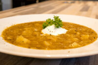 Czech Sauerkraut Soup Zelňačka Bowl of Czech Sauerkraut Soup Zelňačka with diced potatoes, sour cream, and parsley on a wooden table.