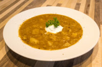 Czech Sauerkraut Soup Zelňačka Bowl of Czech Sauerkraut Soup Zelňačka with diced potatoes, sour cream, and parsley on a wooden table