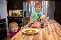 Czech Sauerkraut Soup Zelňačka Bowl of Czech Sauerkraut Soup Zelňačka with sour cream and parsley on a wooden counter, children nearby.