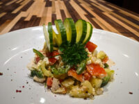 Shopska Salad with diced tomato, cucumber, and feta, topped with a cucumber fan and parsley on a white plate.