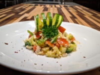 Diced tomato, cucumber, and feta Shopska Salad garnished with cucumber ribbons on a white plate.