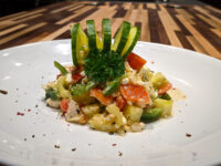 Shopska Salad with diced tomato, feta cubes, and green pepper, topped with a cucumber ribbon curl and parsley.