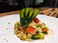 Shopska Salad on a white plate with diced tomato, cucumber, feta, and a fanned cucumber garnish.