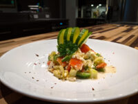 Shopska Salad with diced tomato and feta, plated with a fanned avocado garnish and parsley.